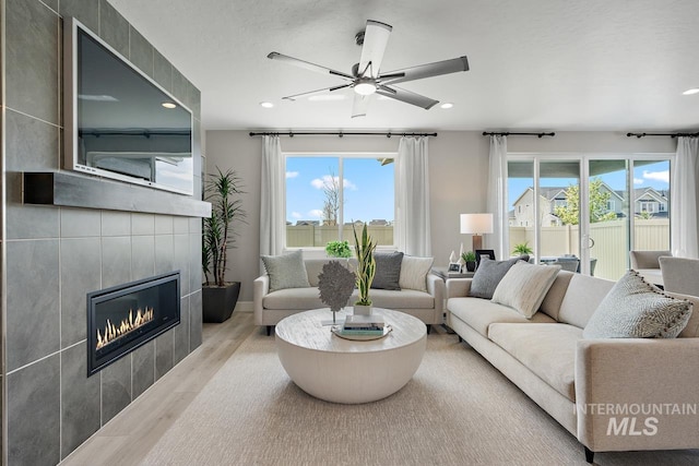 living room with a tile fireplace, hardwood / wood-style flooring, ceiling fan, and a healthy amount of sunlight