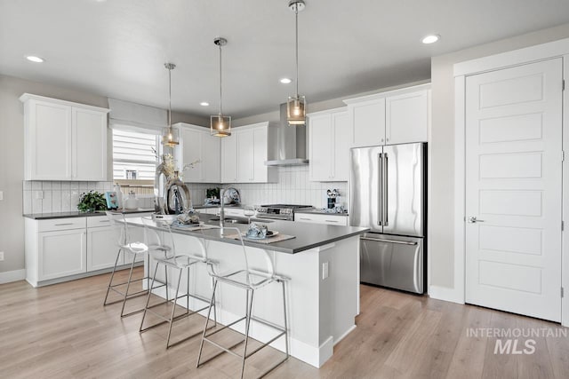 kitchen with wall chimney exhaust hood, premium appliances, a kitchen island, and light hardwood / wood-style floors