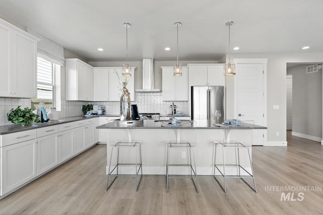 kitchen featuring high end refrigerator, light hardwood / wood-style floors, backsplash, a center island, and wall chimney range hood