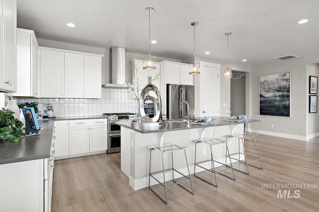 kitchen featuring wall chimney range hood, premium appliances, a center island with sink, and light hardwood / wood-style floors