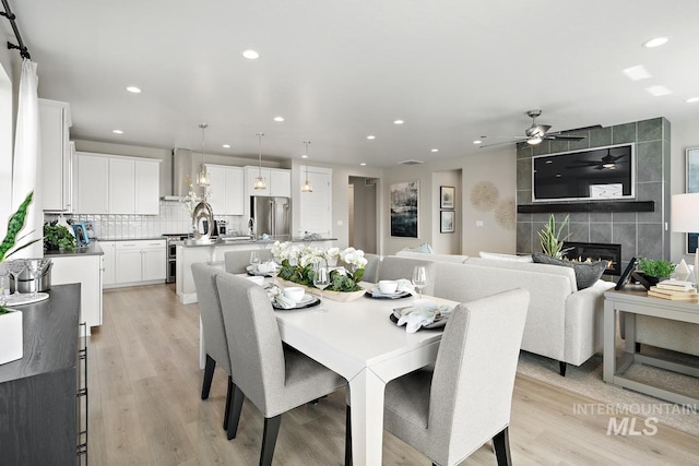 dining area featuring a tile fireplace, light wood-type flooring, and ceiling fan