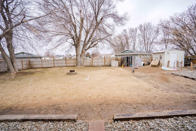 view of yard featuring a fire pit, a storage unit, an outdoor structure, and a fenced backyard