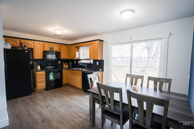 kitchen featuring dark countertops, brown cabinets, wood finished floors, black appliances, and a sink