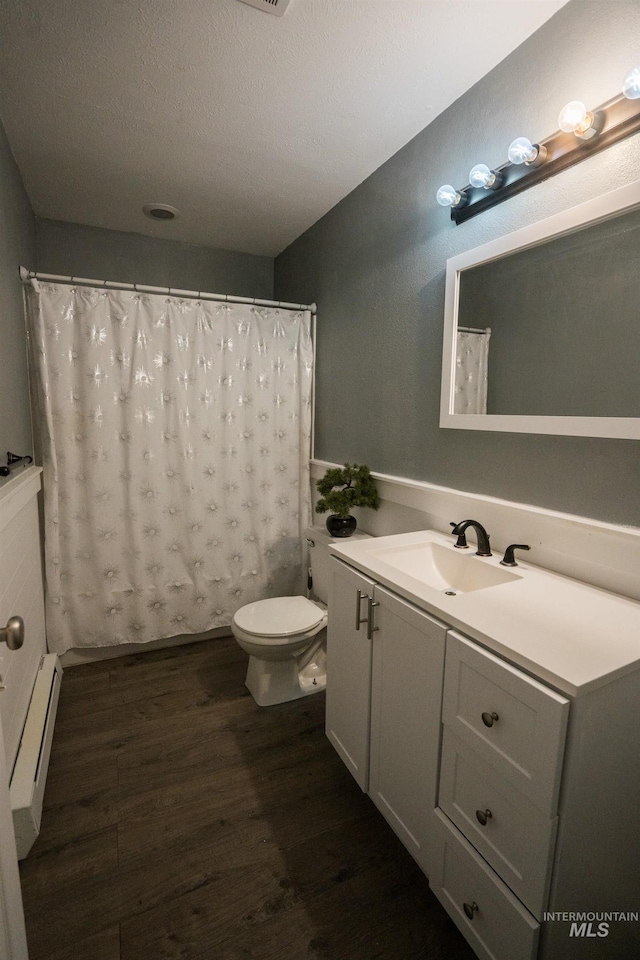 bathroom with a textured ceiling, toilet, a baseboard heating unit, wood finished floors, and vanity