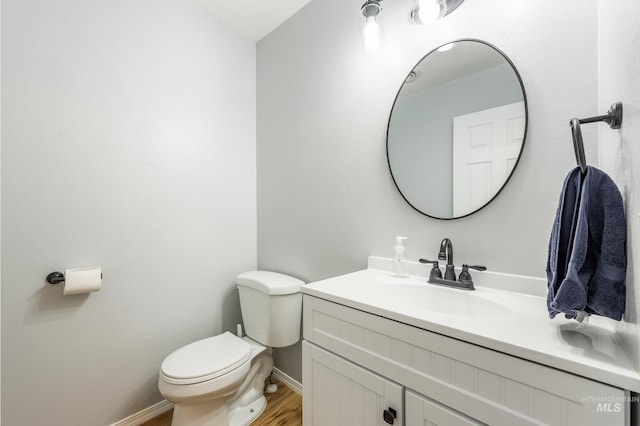 half bathroom with vanity, toilet, wood finished floors, and baseboards