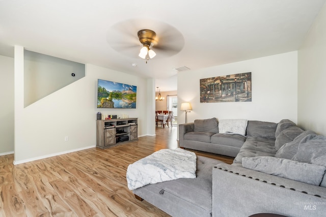 living room featuring baseboards, ceiling fan with notable chandelier, visible vents, and light wood finished floors