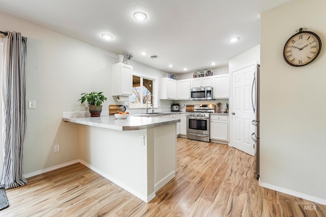 kitchen with light wood-style flooring, appliances with stainless steel finishes, a peninsula, white cabinets, and a sink