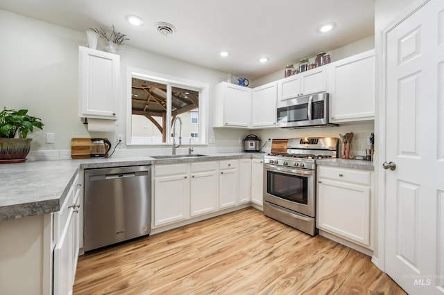 kitchen featuring visible vents, a sink, appliances with stainless steel finishes, white cabinets, and light wood finished floors