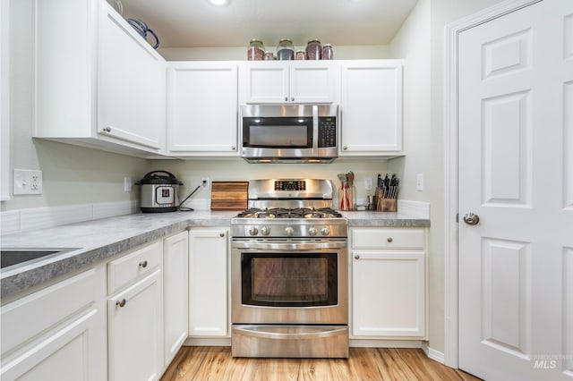 kitchen featuring light wood finished floors, appliances with stainless steel finishes, white cabinetry, and light countertops