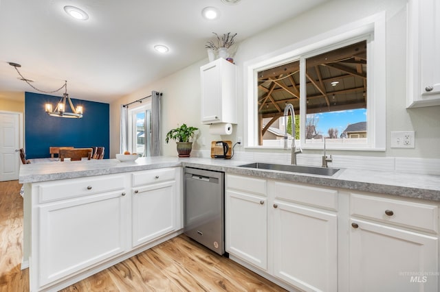 kitchen featuring light wood-style flooring, a sink, stainless steel dishwasher, a peninsula, and white cabinets