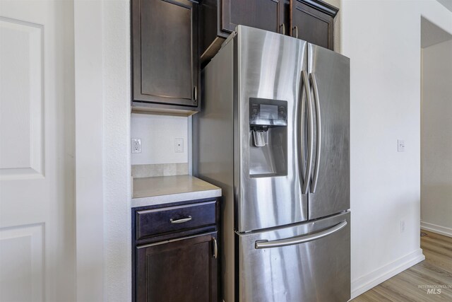 kitchen with light wood-style floors, stainless steel fridge with ice dispenser, dark brown cabinets, light countertops, and baseboards