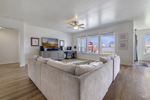 living room featuring wood finished floors, baseboards, a ceiling fan, and visible vents
