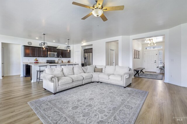 living room with baseboards, light wood finished floors, recessed lighting, and ceiling fan with notable chandelier