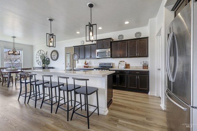 kitchen featuring a sink, light countertops, appliances with stainless steel finishes, a kitchen breakfast bar, and light wood-style flooring