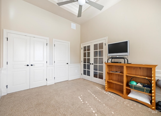 unfurnished bedroom with a wainscoted wall, visible vents, carpet floors, high vaulted ceiling, and french doors