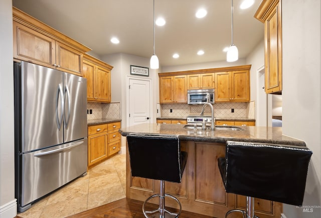 kitchen with dark stone countertops, a peninsula, a sink, appliances with stainless steel finishes, and pendant lighting