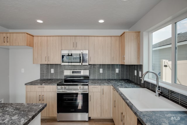 kitchen with light brown cabinets, sink, stainless steel appliances, and dark stone counters