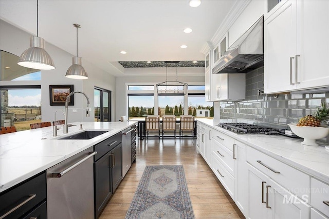 kitchen featuring a sink, decorative backsplash, stainless steel appliances, white cabinetry, and wall chimney range hood