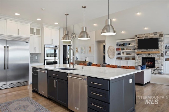 kitchen with a sink, open floor plan, wood finished floors, stainless steel appliances, and white cabinets