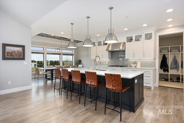 kitchen featuring light wood-style flooring, a sink, tasteful backsplash, gas stovetop, and wall chimney exhaust hood