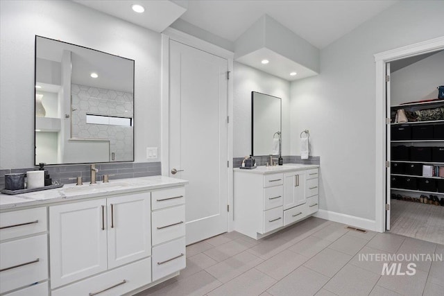 bathroom featuring baseboards, visible vents, tiled shower, two vanities, and a sink