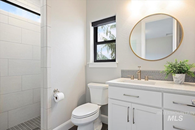 full bath featuring vanity, toilet, baseboards, and tiled shower