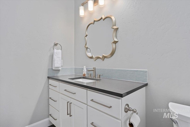 bathroom featuring toilet, vanity, and a textured wall