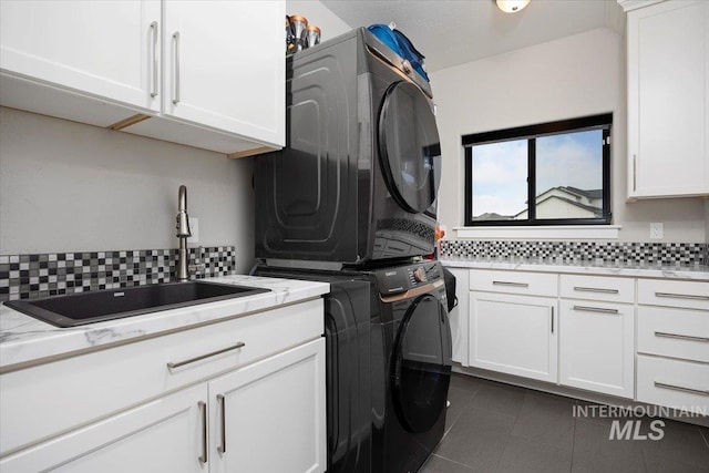 laundry room featuring dark tile patterned flooring, cabinet space, stacked washer and clothes dryer, and a sink