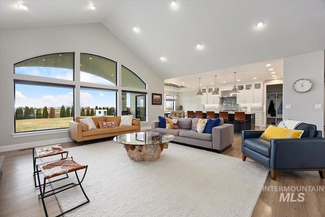 living area with recessed lighting, baseboards, light wood-style floors, and high vaulted ceiling