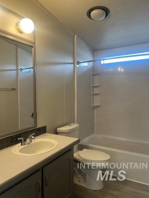 bathroom featuring vanity, wood finished floors, shower / washtub combination, a textured ceiling, and toilet