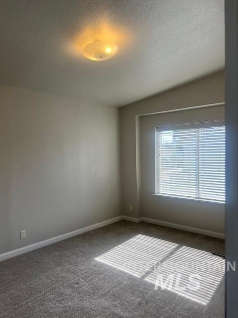 unfurnished room with dark carpet, a textured ceiling, and baseboards