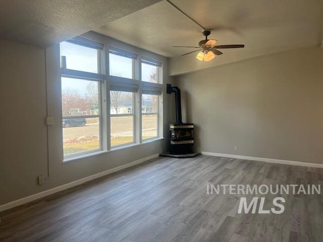 unfurnished living room featuring ceiling fan, baseboards, a wood stove, wood finished floors, and a textured ceiling