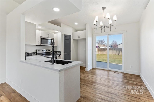 kitchen with stainless steel appliances, white cabinets, decorative light fixtures, light hardwood / wood-style floors, and kitchen peninsula