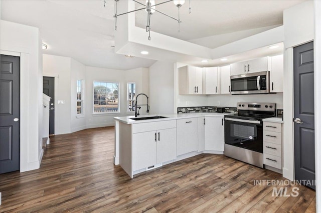 kitchen with kitchen peninsula, dark hardwood / wood-style floors, stainless steel appliances, white cabinetry, and sink