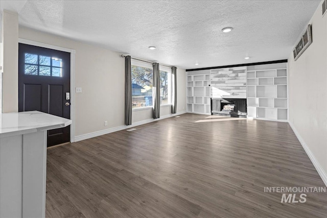 unfurnished living room with a large fireplace, a textured ceiling, dark hardwood / wood-style flooring, and built in shelves