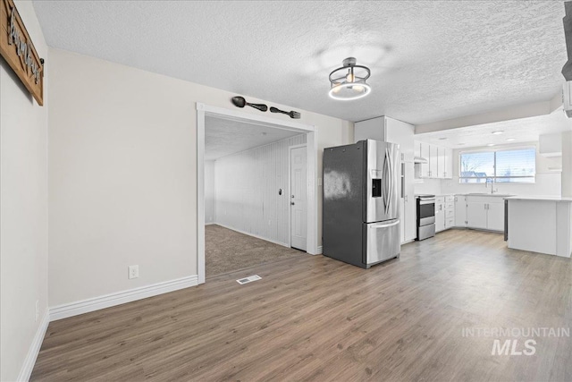 kitchen with appliances with stainless steel finishes, white cabinetry, sink, light wood-type flooring, and a textured ceiling