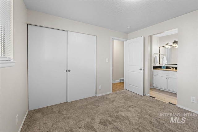 unfurnished bedroom with ensuite bath, light carpet, a textured ceiling, and a closet