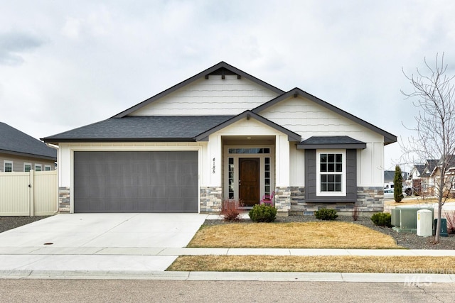 view of front of house with stone siding, roof with shingles, driveway, and fence