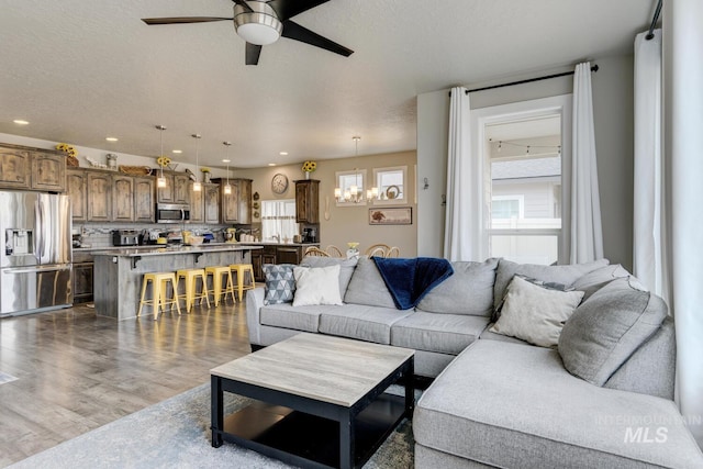 living room with dark wood finished floors, recessed lighting, ceiling fan with notable chandelier, and a textured ceiling