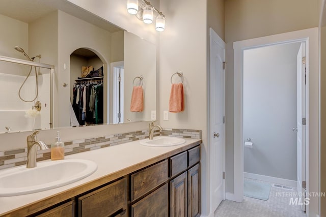 bathroom with double vanity, decorative backsplash, a shower, and a sink