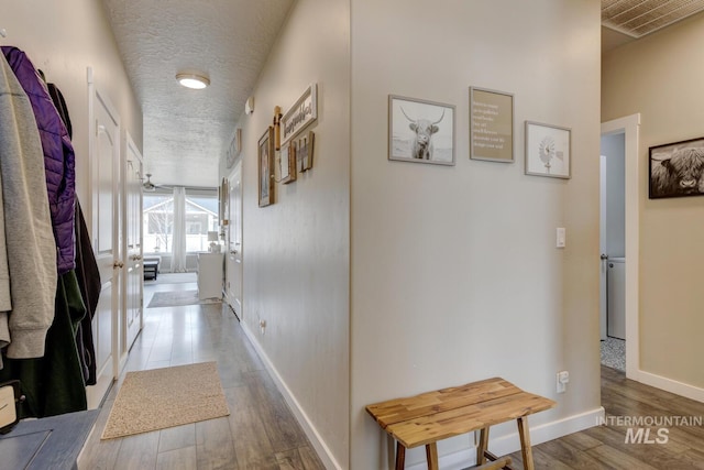 hall featuring visible vents, baseboards, a textured ceiling, and wood finished floors