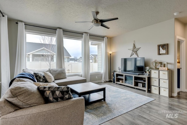 living area featuring baseboards, a textured ceiling, wood finished floors, and a ceiling fan