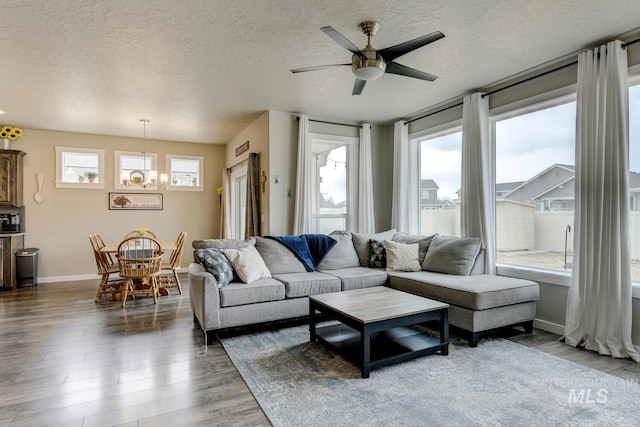 living area featuring ceiling fan with notable chandelier, a textured ceiling, baseboards, and wood finished floors