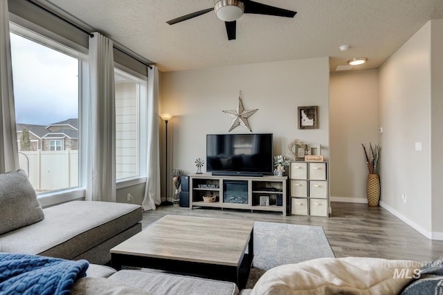 living room featuring baseboards, a textured ceiling, a ceiling fan, and wood finished floors