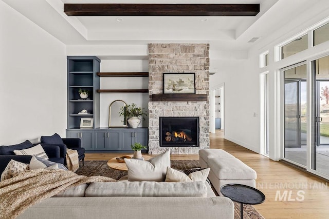 living room with light hardwood / wood-style floors, a stone fireplace, and built in features