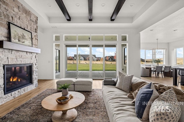 living room with beam ceiling, a stone fireplace, and hardwood / wood-style floors