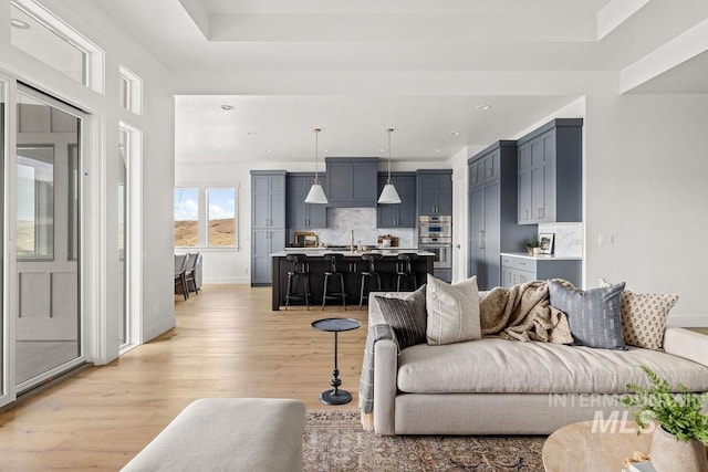 living room featuring a tray ceiling, sink, and light wood-type flooring