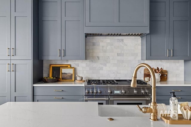 kitchen with tasteful backsplash, gray cabinets, light stone countertops, and high end range