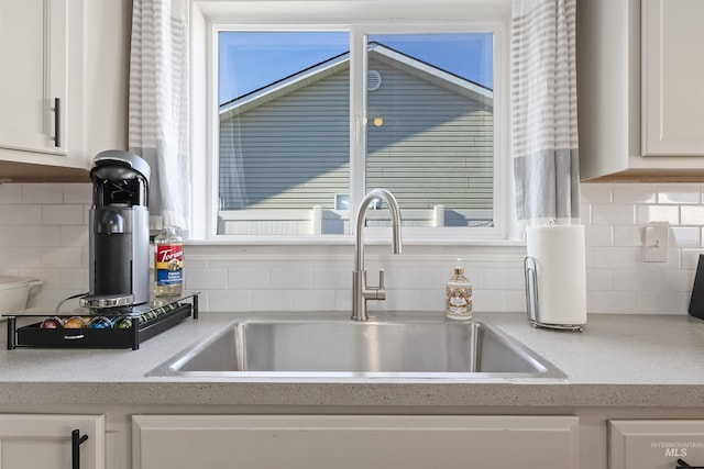 details featuring tasteful backsplash, white cabinetry, light stone countertops, and sink