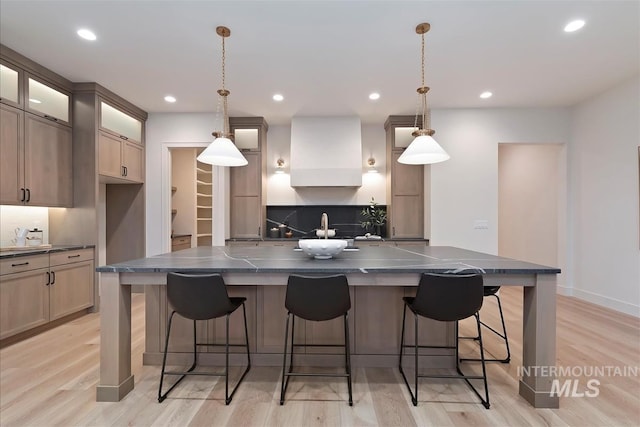 9989 W Bouvardia St, Star, ID 83699 - kitchen with dark countertops, glass insert cabinets, wall chimney range hood, light wood-style flooring, and recessed lighting